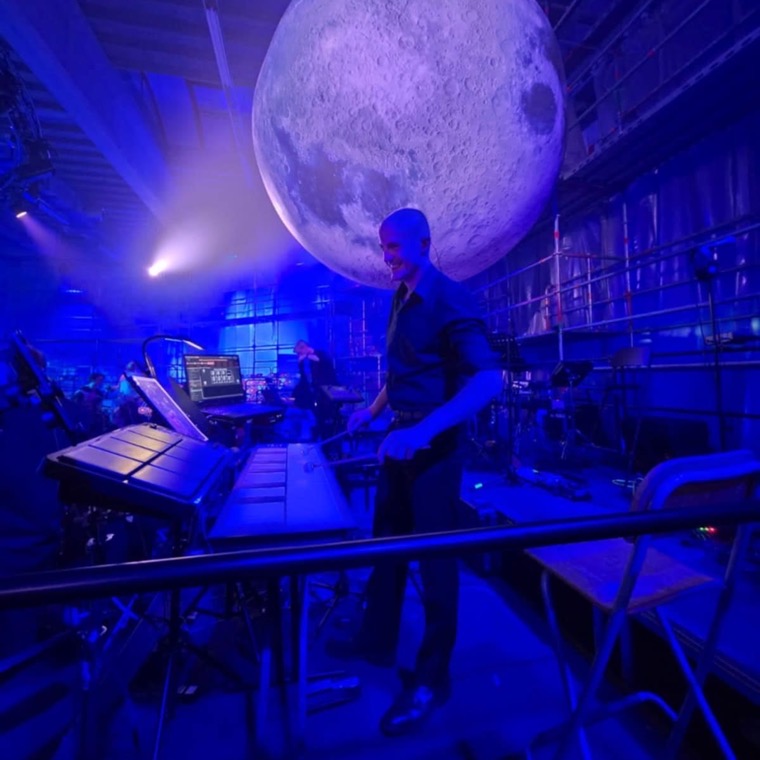 Dennis Vanhove achter klavierpercussie op een podium in blauw licht, met een grote maanbol boven de scène.